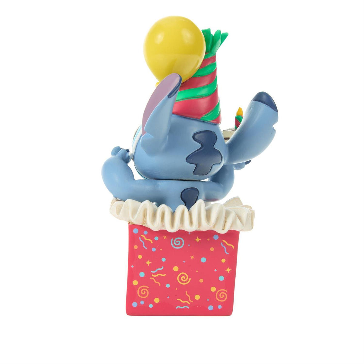 Stitch popping out of a present wearing a birthday hat and holding a piece of cake