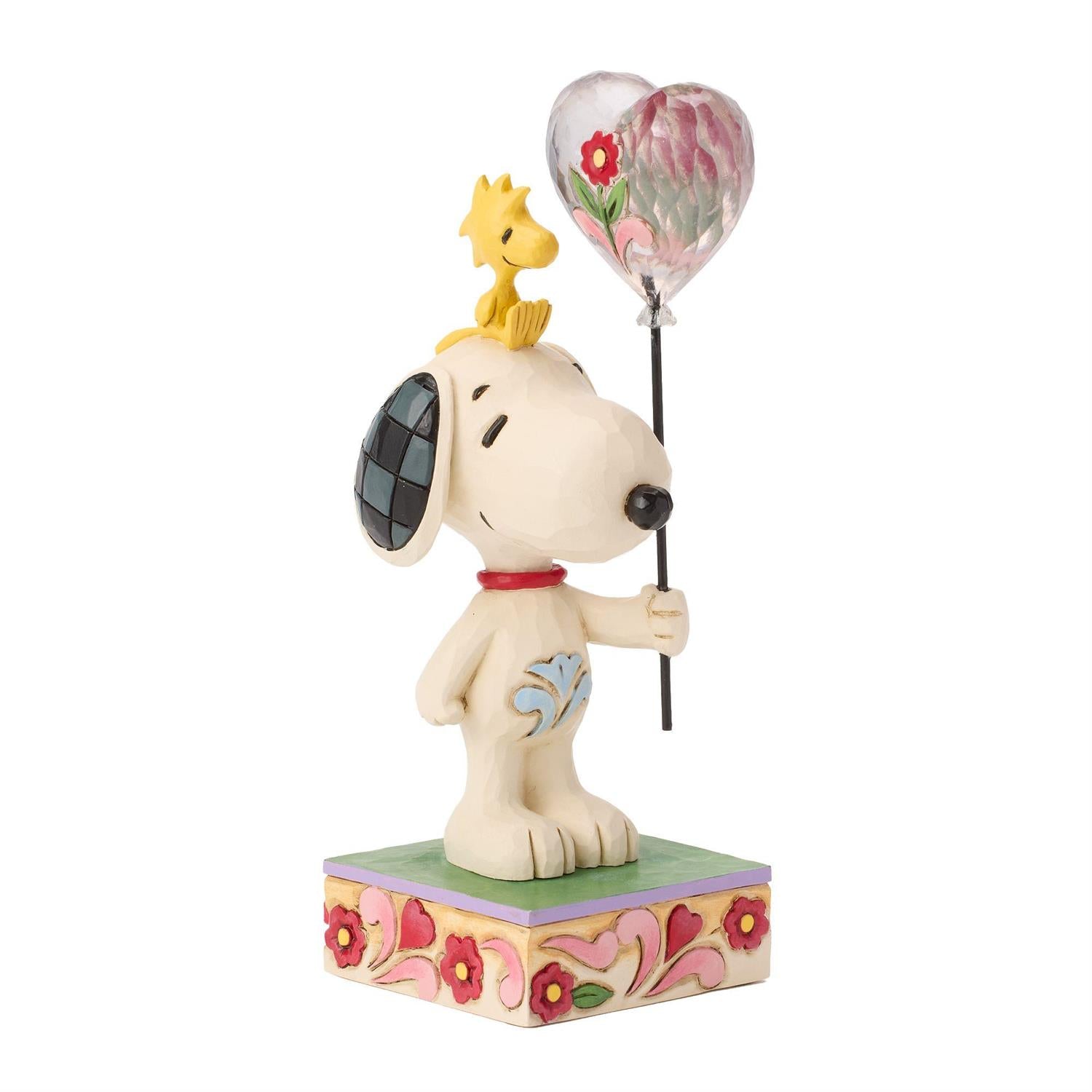 Snoopy holding a heart balloon while Woodstock sitting on his head