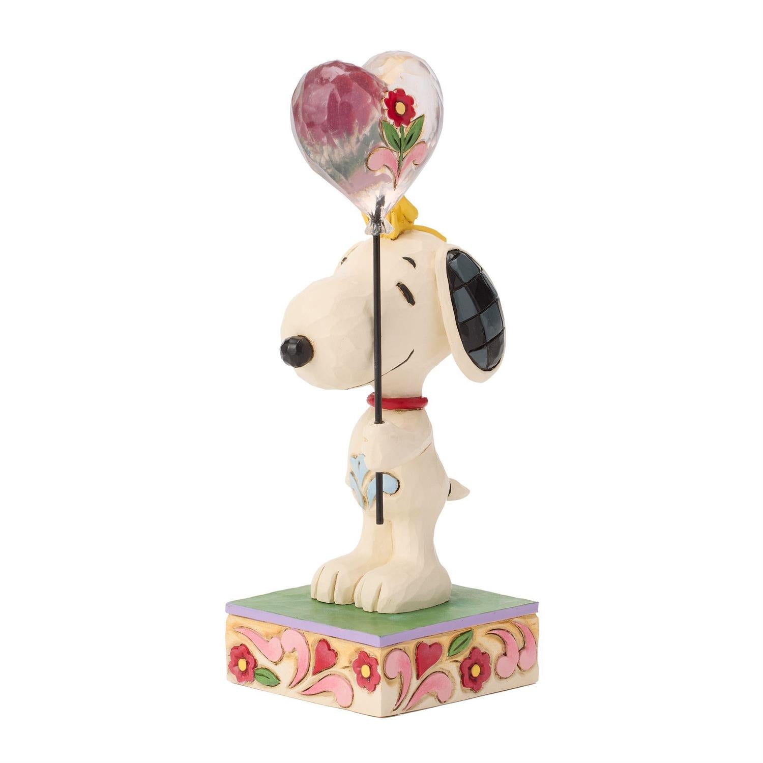 Snoopy holding a heart balloon while Woodstock sitting on his head